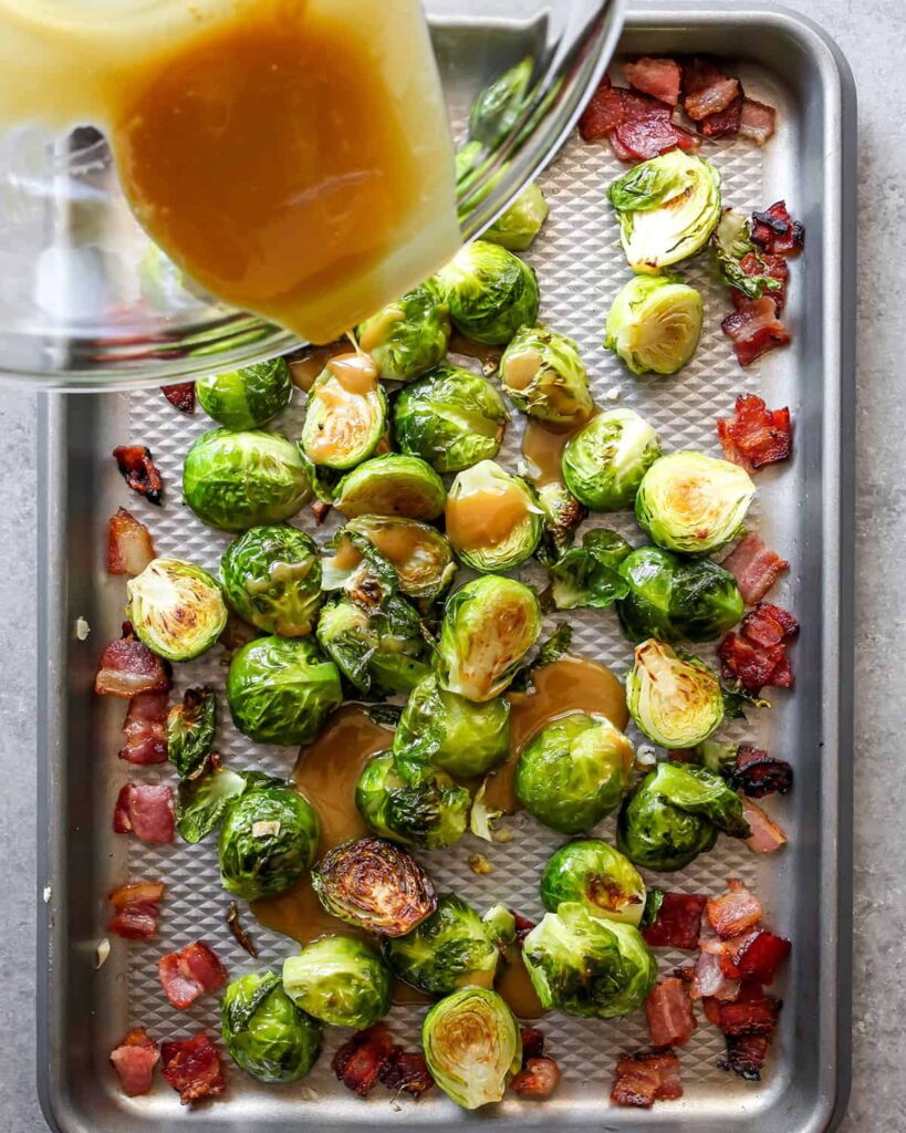 Roasted Brussels sprouts with bacon and sauce on a baking sheet, perfect for a savory side dish.