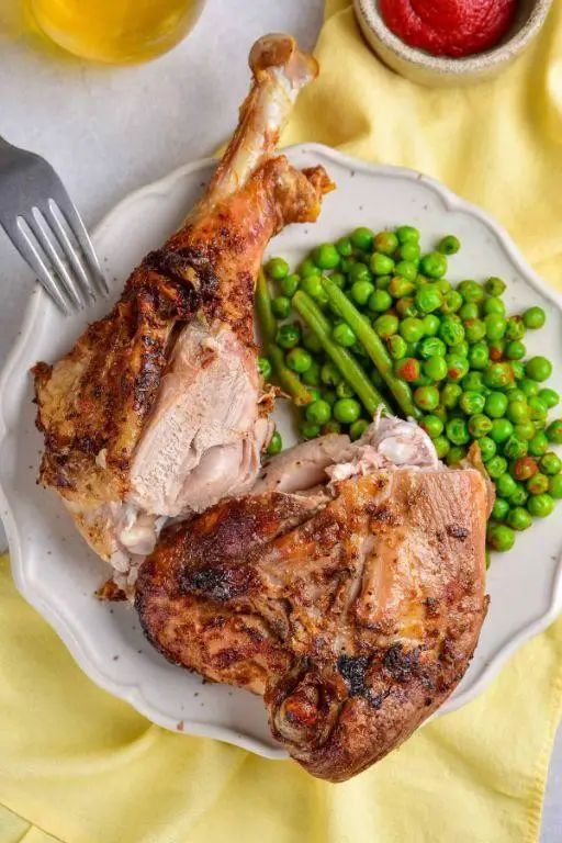 Roasted turkey legs served with peas and green beans on a white plate, perfect for dinner.