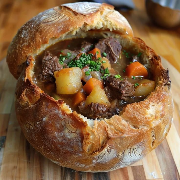 Hearty beef stew served in a rustic bread bowl with potatoes and carrots on a wooden table.