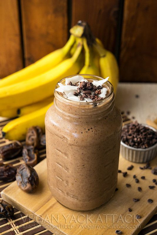 Creamy chocolate banana smoothie in a mason jar, garnished with coconut flakes and cacao nibs, surrounded by bananas.