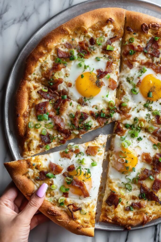 Breakfast pizza with sunny-side-up eggs, bacon, and green onions, served on a tray, hand holding a slice.