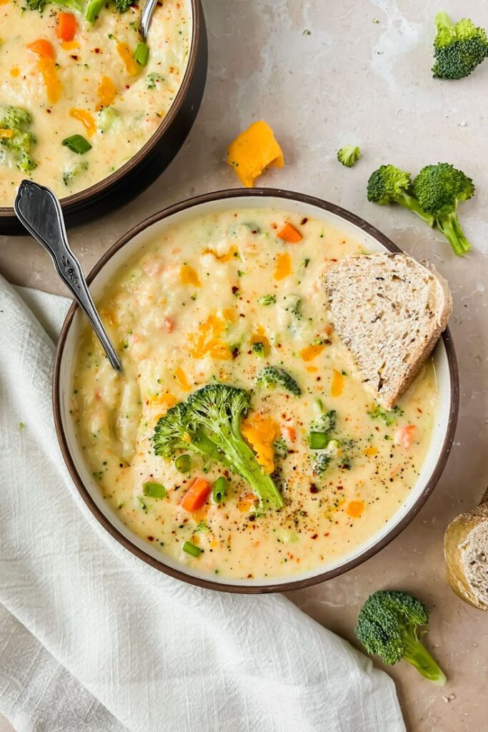 Broccoli White Cheddar Soup - The Ultimate Creamy Broccoli Cheddar Soup: A Cozy Classic | Creamy broccoli cheddar soup with fresh vegetables and bread slice on a table setting.