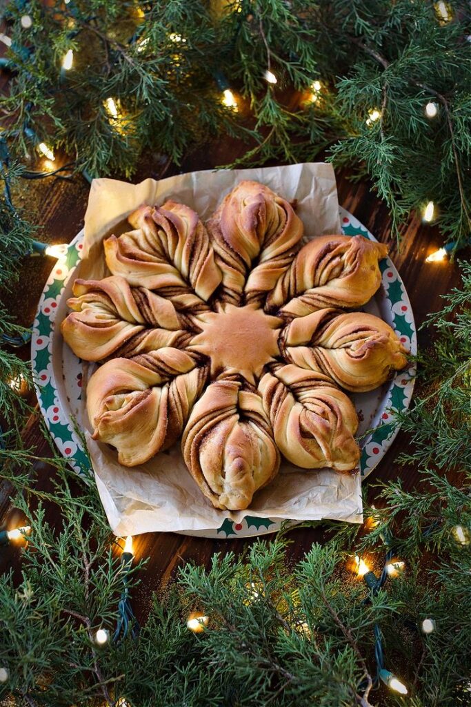 Christmas Cinnamon Star Bread Recipe _ Made for Gifting - Bake Some Magic! Festive Christmas Star Cinnamon Rolls | Decorative cinnamon star bread on a festive plate, surrounded by greenery and lights, perfect for holiday gatherings.