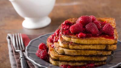 Stack of French toast topped with fresh raspberries and syrup on a gray plate.