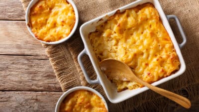 Creamy baked mac and cheese in a casserole with a wooden spoon on rustic wooden table, ready to serve.