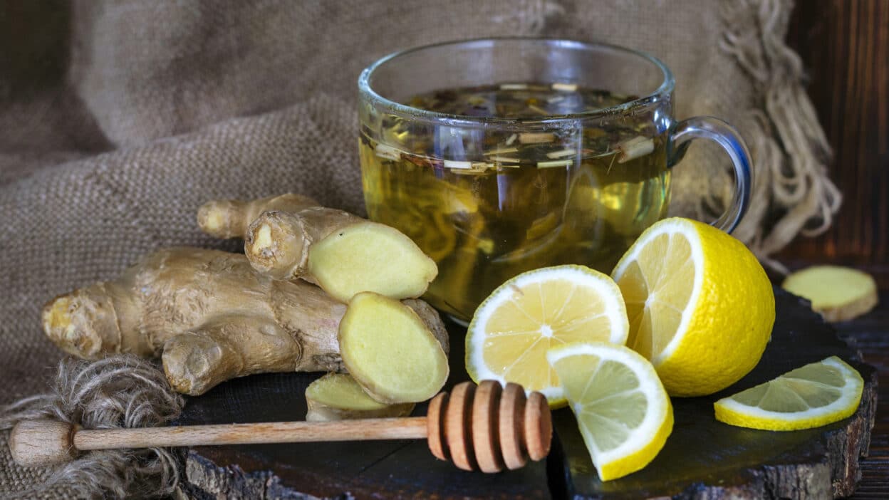 Cup of ginger tea with sliced lemon and fresh ginger on rustic wood, emphasizing natural wellness ingredients.