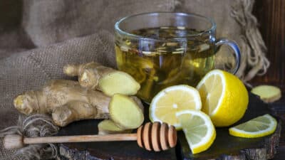 Cup of ginger tea with sliced lemon and fresh ginger on rustic wood, emphasizing natural wellness ingredients.