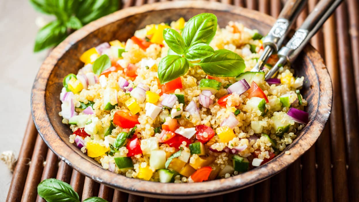 Colorful quinoa salad with diced vegetables and basil garnish in a wooden bowl.