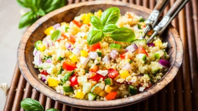 Colorful quinoa salad with diced vegetables and basil garnish in a wooden bowl.