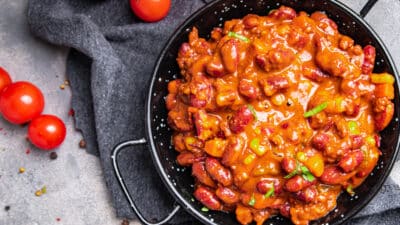 Hearty chili con carne in a black bowl garnished with fresh herbs, surrounded by cherry tomatoes and spices.