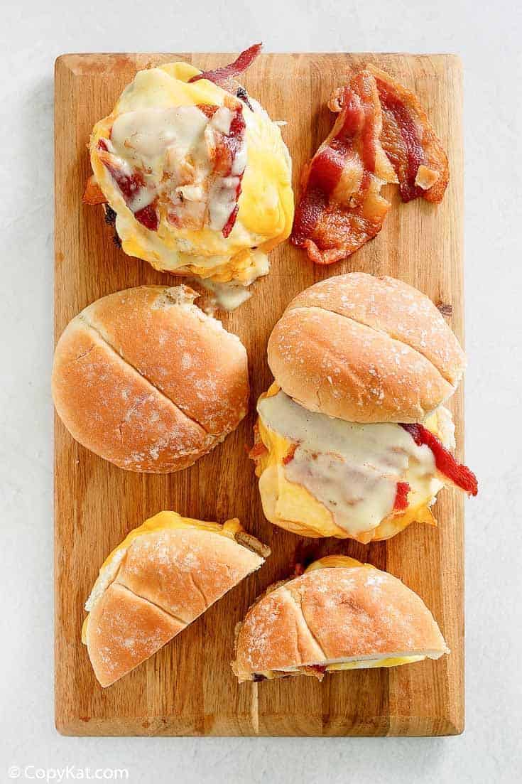 Breakfast sandwiches with bacon, egg, and cheese on a wooden board, perfect for a hearty morning meal.