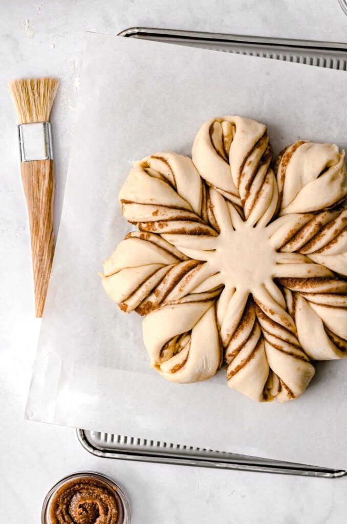 Overnight Buttermilk Cinnamon Star Bread - Bake Some Magic! Festive Christmas Star Cinnamon Rolls | Star-shaped cinnamon pastry dough on parchment paper, ready to bake, next to a brush and cinnamon filling.