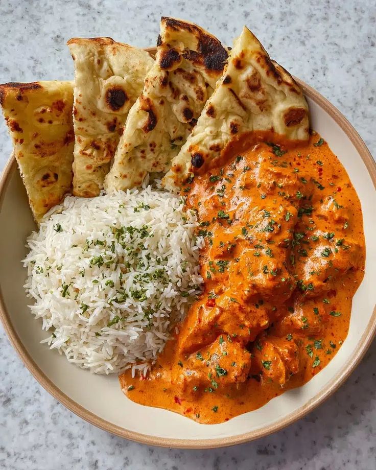 Quick Easy Homemade Butter Chicken Recipe - Flavorful Indian Delight - Homemade Butter Chicken: Easy, Creamy, Authentic Recipe - Chief Stories Creamy butter chicken with naan and rice, garnished with herbs on a marble table. Perfect for an Indian cuisine feast.