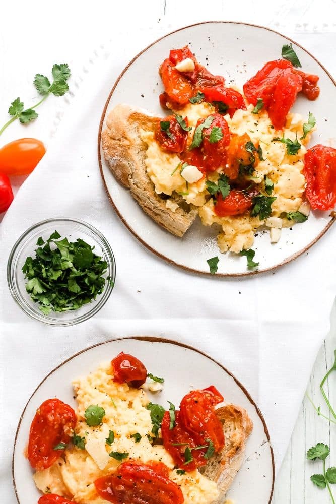 Scrambled Eggs with Tomatoes Cheese Cilantro - Happy Veggie Kitchen - Cheesy Tomato Scramble: Quick & Delicious Breakfast - Chief Stories Scrambled eggs on toast with roasted tomatoes and herbs for breakfast, served on white plates with chopped cilantro.