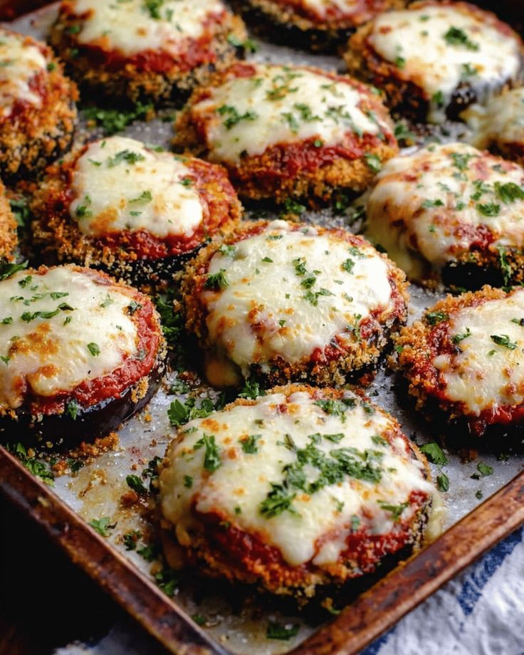 Baked eggplant slices topped with melted cheese, tomato sauce, and herbs on a tray. Delicious vegetarian dish.