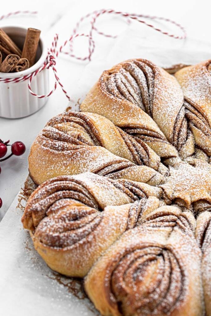 Sourdough cinnamon star bread | adventuresinfoodielandcom - Bake Some Magic! Festive Christmas Star Cinnamon Rolls | Festive cinnamon twist bread with powdered sugar, with cinnamon sticks and cranberries in the background.