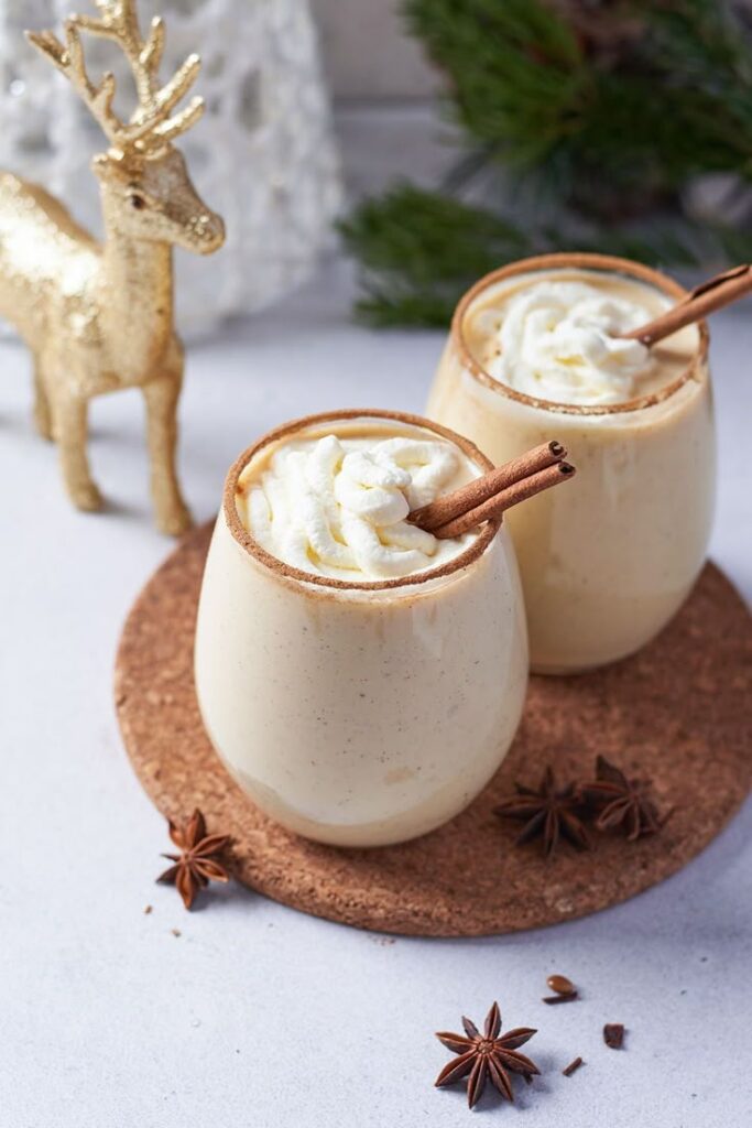 Virgin Eggnog Mocktail Recipe - Mocktail_net - 5 Best Christmas Drinks: Festive Sips for Holidays Festive holiday eggnog with whipped cream and cinnamon sticks in glasses, surrounded by star anise and decorations.