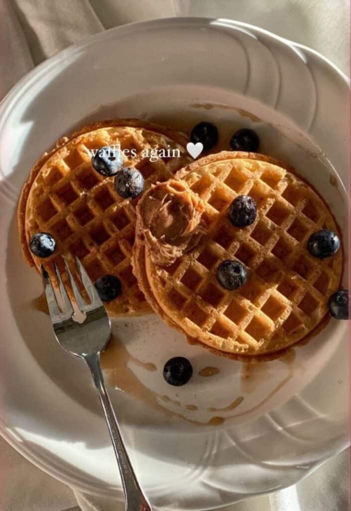 Plate of waffles with blueberries and a dollop of peanut butter, served with a fork. Delicious breakfast treat.