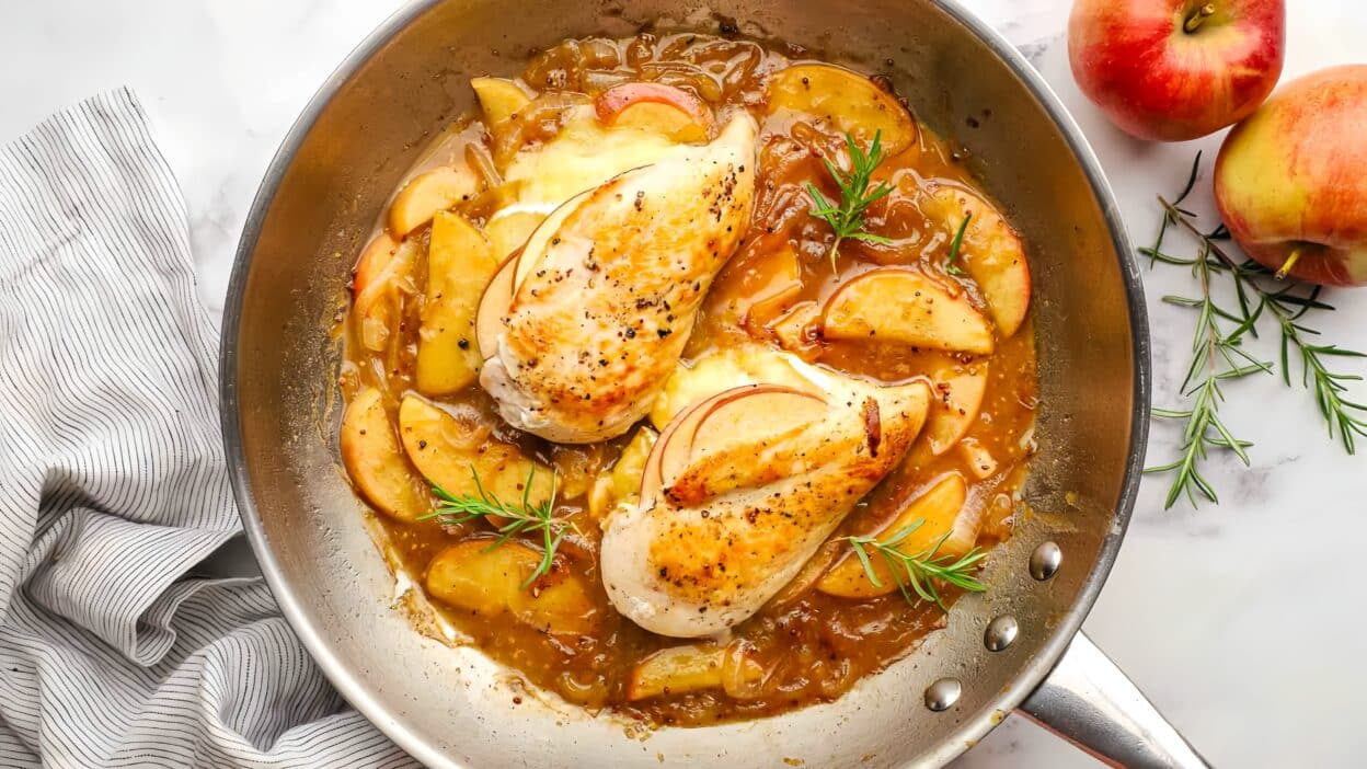 Pan-seared chicken with apple slices and rosemary in savory sauce, garnished with fresh herbs.