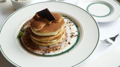 Delicious stack of pancakes topped with cocoa and a chocolate piece on a white plate, ready to enjoy.
