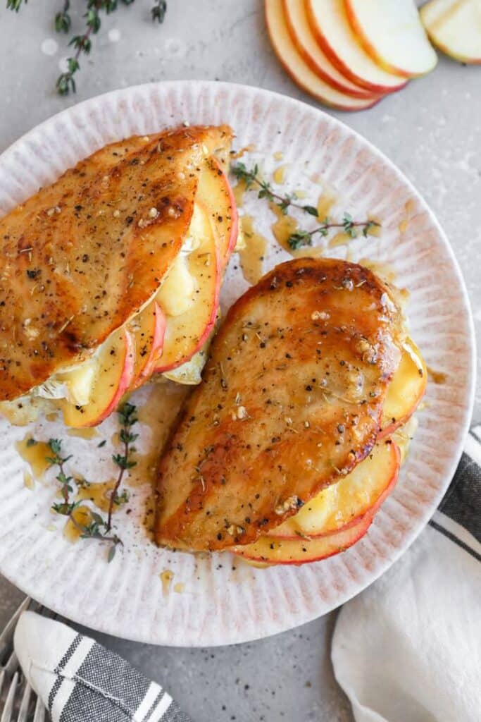 Grilled chicken stuffed with apples and cheese on a plate, garnished with thyme and honey drizzle.