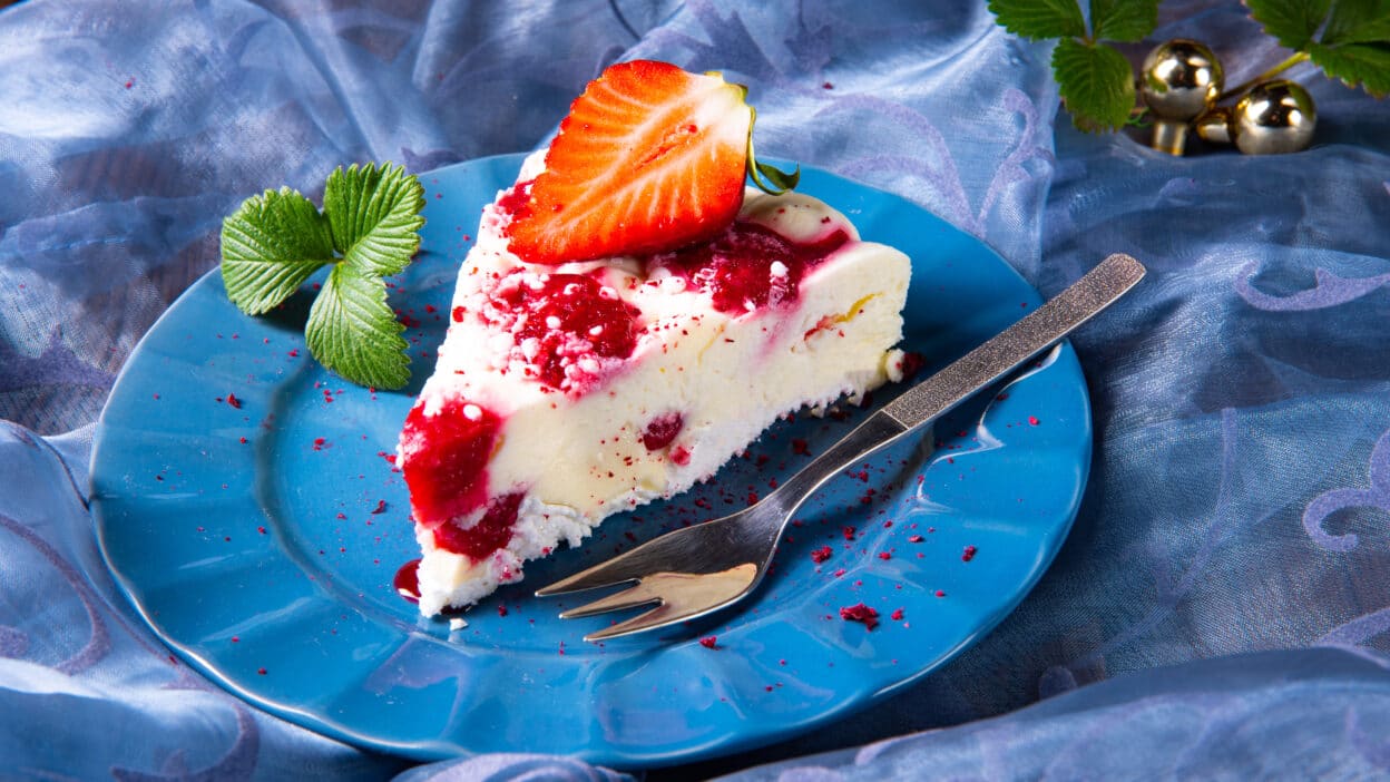 Slice of cheesecake with strawberry topping on a blue plate, garnished with fresh mint leaves.