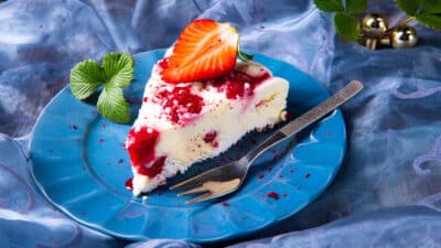 Slice of cheesecake with strawberry topping on a blue plate, garnished with fresh mint leaves.
