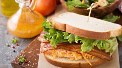 BLT sandwich with crispy bacon, fresh lettuce, and cheese spread on a wooden board, served with salad and dressing.