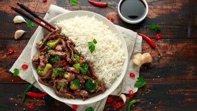 Plate of beef stir fry with broccoli and white rice on a rustic table with chopsticks and soy sauce.