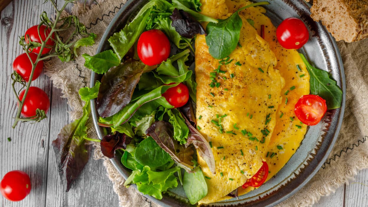 Delicious omelette with fresh greens and cherry tomatoes on a rustic plate, perfect for a healthy breakfast.