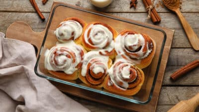 Freshly baked cinnamon rolls with creamy icing in a glass dish on a wooden board.