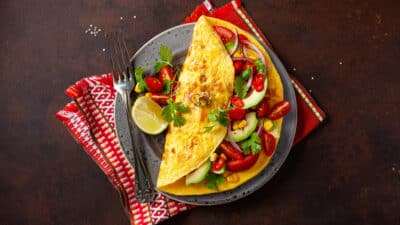 Colorful vegetable omelette with tomatoes, avocado, corn, and cilantro on a plate with lime wedge.