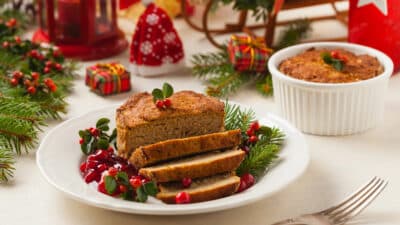 Festive table with sliced meatloaf, cranberry sauce, and holiday decorations in a cozy, Christmas setting.