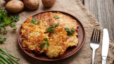 Plate of golden potato pancakes garnished with parsley on a rustic table, surrounded by fresh ingredients.