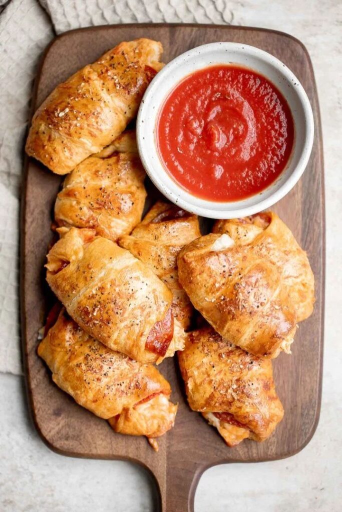 Cheesy pepperoni pizza rolls with marinara sauce on a wooden board, perfect for a tasty appetizer or snack.