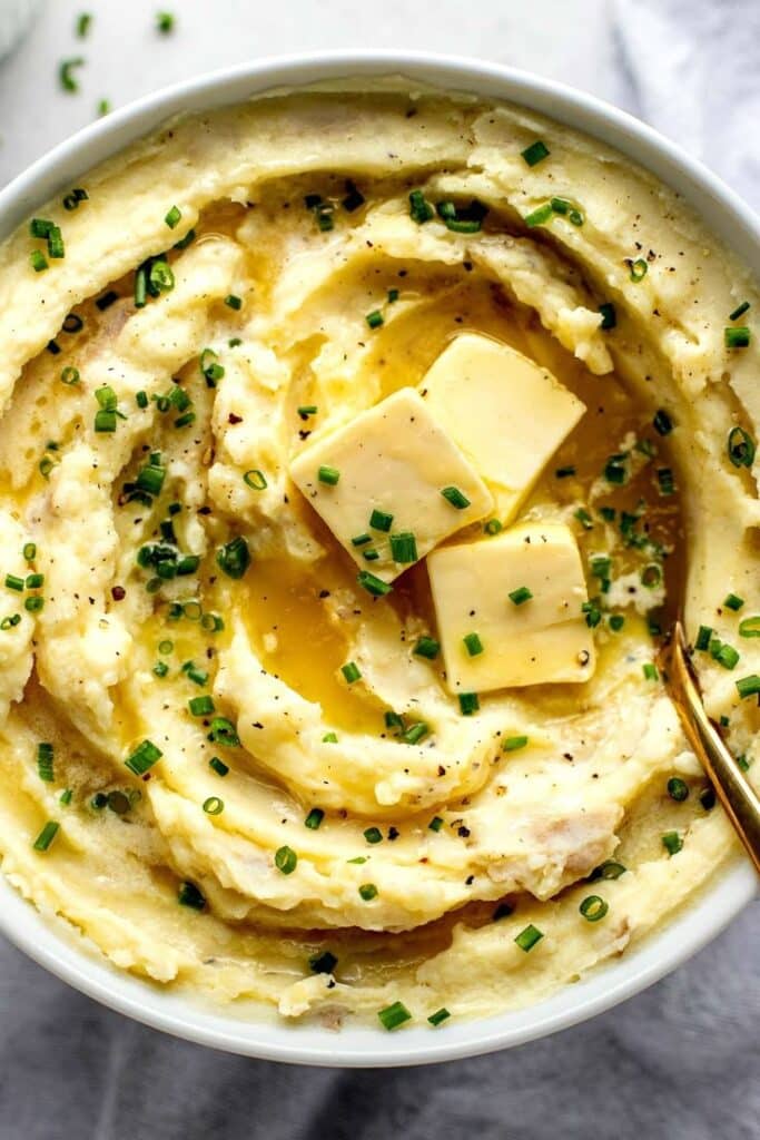 Creamy mashed potatoes topped with butter and chives in a white bowl.