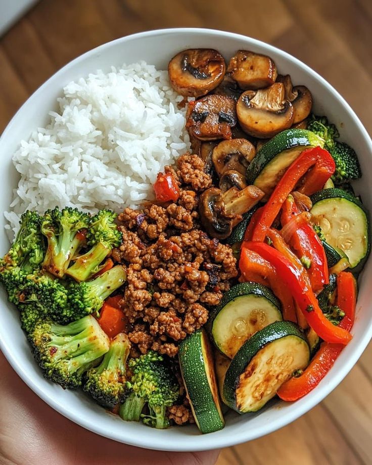 Healthy rice bowl with sautéed mushrooms, zucchini, bell peppers, broccoli, and seasoned ground meat.