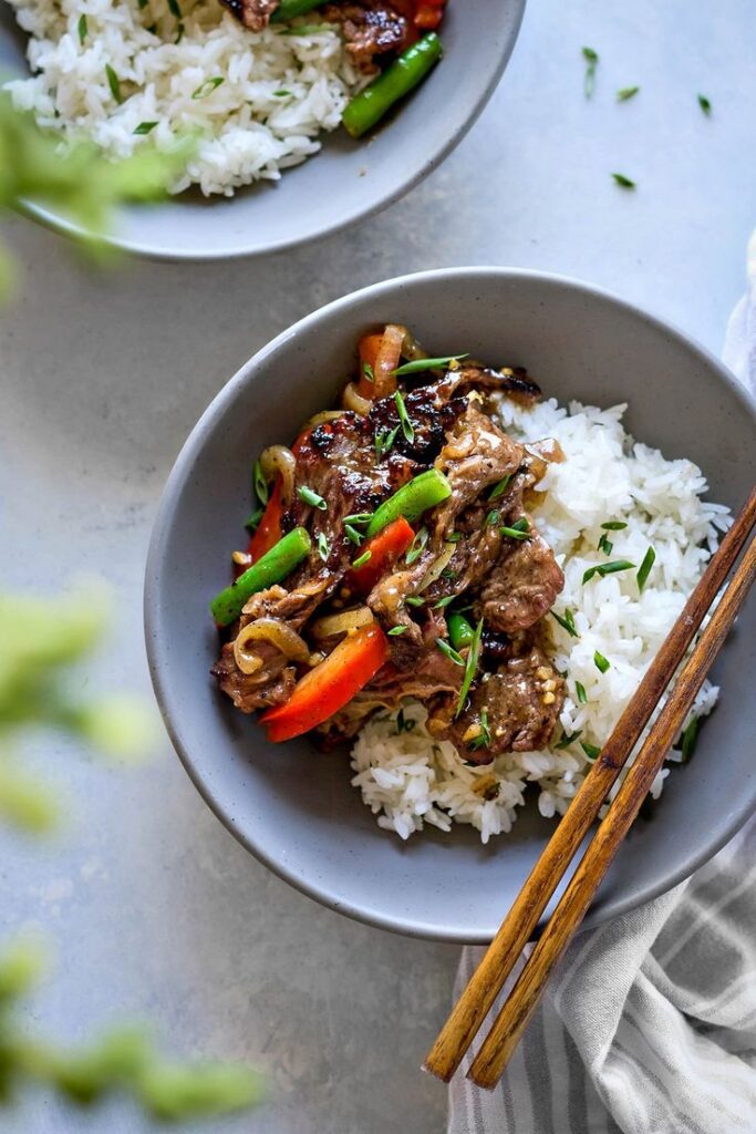 Stir-fried beef with colorful vegetables over fluffy white rice in a bowl. Asian cuisine meal, served with chopsticks.