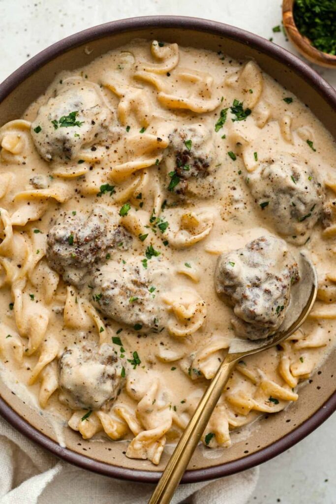 Creamy Swedish meatballs with pasta in a rich sauce, garnished with parsley in a bowl. Comfort food at its finest.