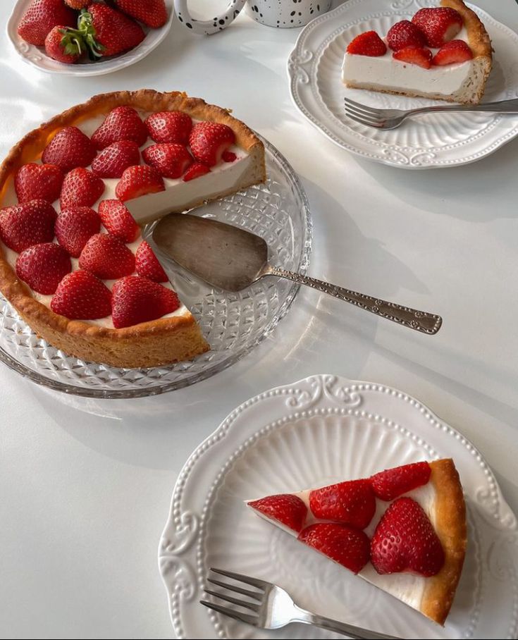 Strawberry cheesecake with slices on plates, featuring fresh strawberries on a glass platter and white tableware.