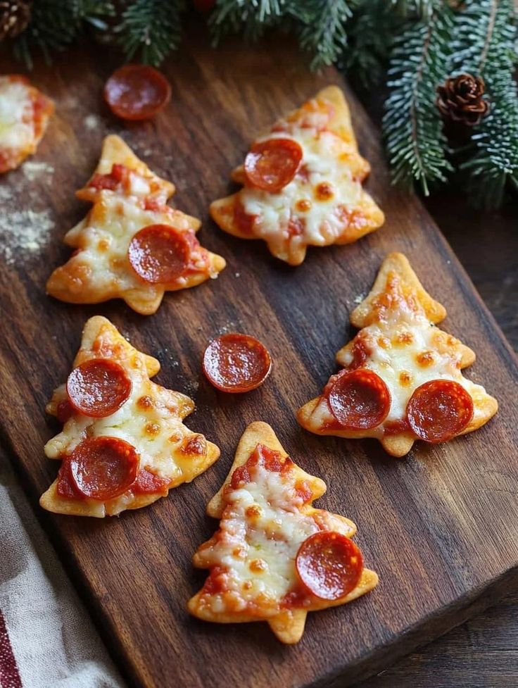 Christmas tree-shaped mini pepperoni pizzas on a wooden board, garnished with festive greens. Christmas Tree Mini Pizzas 