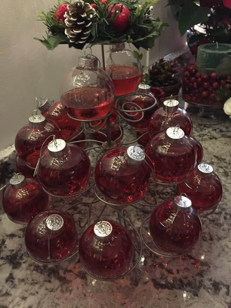 _ - 2025-12-05T100754407 - Celebrate in Style: Festive Ornament Cocktails for Holidays Red liquid-filled Christmas ornaments arranged on a decorative wire stand, topped with festive greenery.