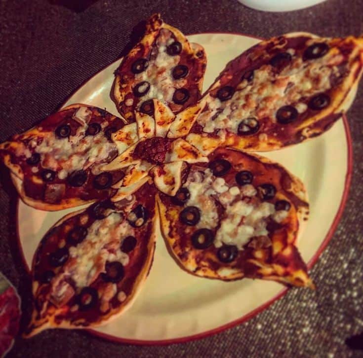 _ - 2025-12-05T105242525 - Demogorgon Pizza Recipe: Stranger Things Food Fun Creative flower-shaped pizza with olives and cheese on a white plate.