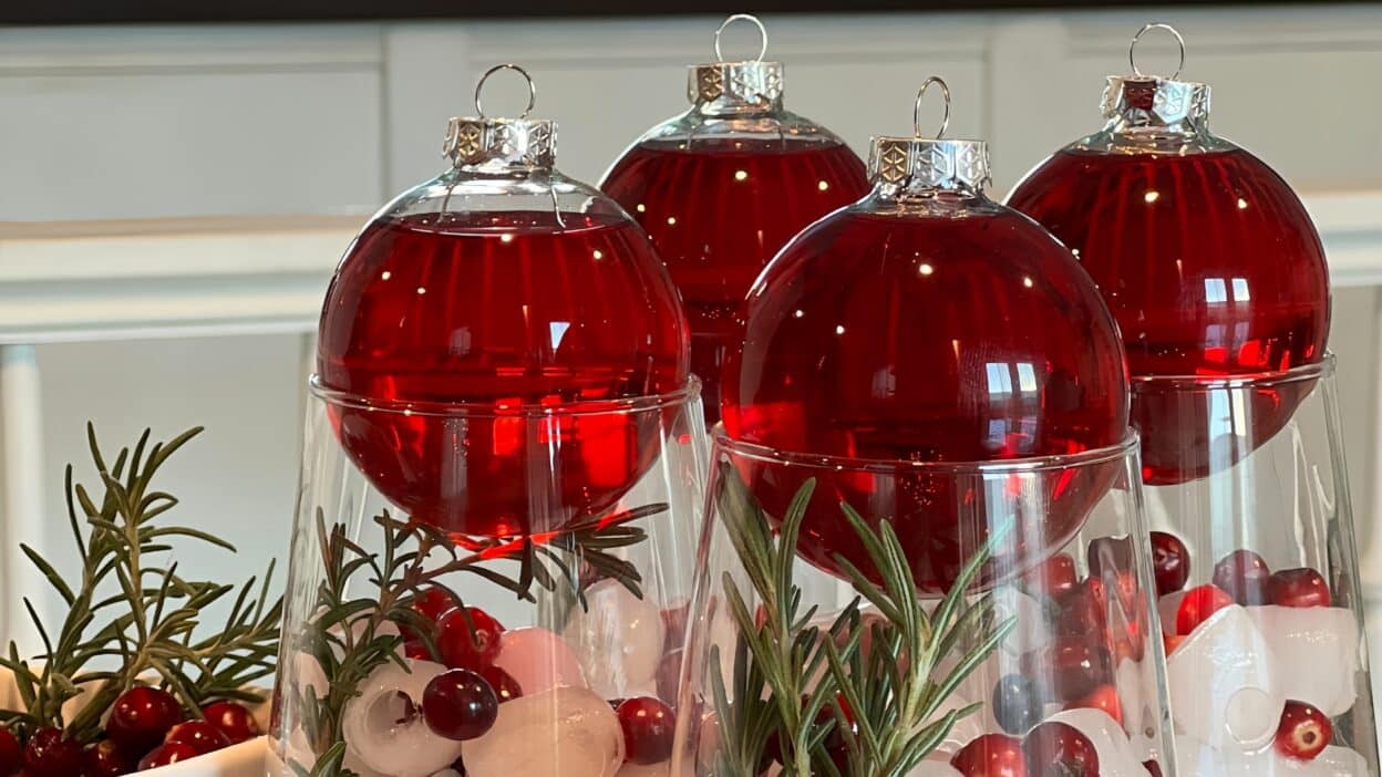Red Christmas ornaments in glasses with cranberries and rosemary, festive holiday decor on display.