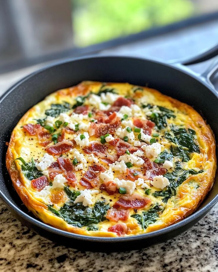Bacon-Spinach-Feta Frittata - SimplyYummyBites - Easy Christmas Breakfast Recipes for Joyful Mornings Delicious spinach bacon frittata in a skillet, topped with crumbled cheese and chives, ready to serve.