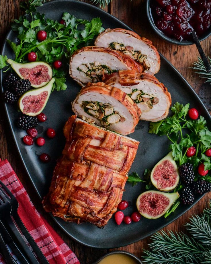 Bacon-wrapped stuffed turkey roll with figs and fresh herbs on a festive plate, garnished with berries and parsley.