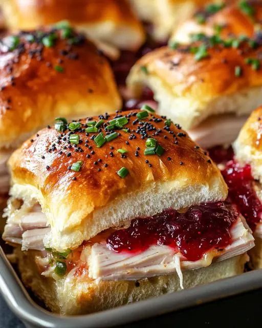 Tasty turkey sliders with cranberry sauce on fluffy buns, garnished with chives and poppy seeds, perfect for a holiday meal.
