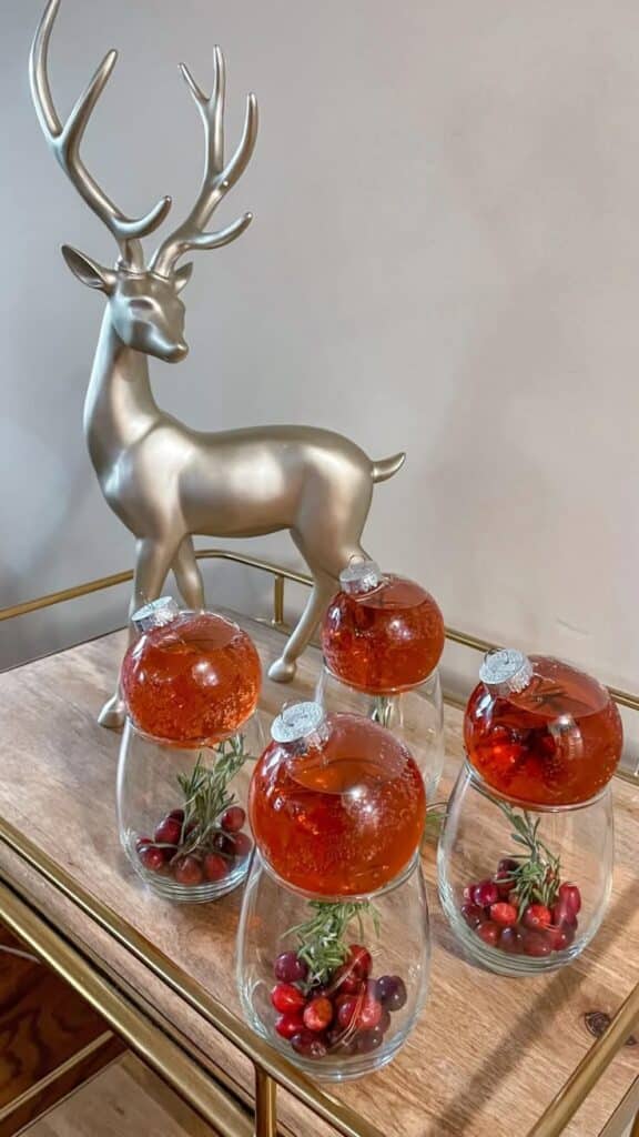 Christmas Ornament Cocktails - Helen G_ Bailey - Celebrate in Style: Festive Ornament Cocktails for Holidays Silver reindeer decor with festive drink ornaments and cranberries on a wooden table.