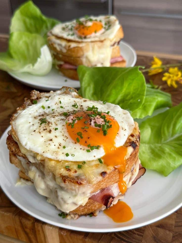 Classic Croque Madame Sandwich - Season Serve - Insider Tips for a Delicious, Gourmet Croque Madame Delicious croque madame sandwich with melted cheese and sunny-side-up egg, garnished with greens on a wooden table.