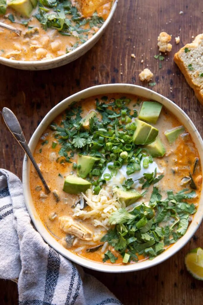 Creamy White Chicken Chili_ - Your Guide to Delicious White Chicken Chili with Easy Tips Creamy chicken soup with avocado, cilantro, cheese, and green onions, served in a bowl on a rustic wooden table.